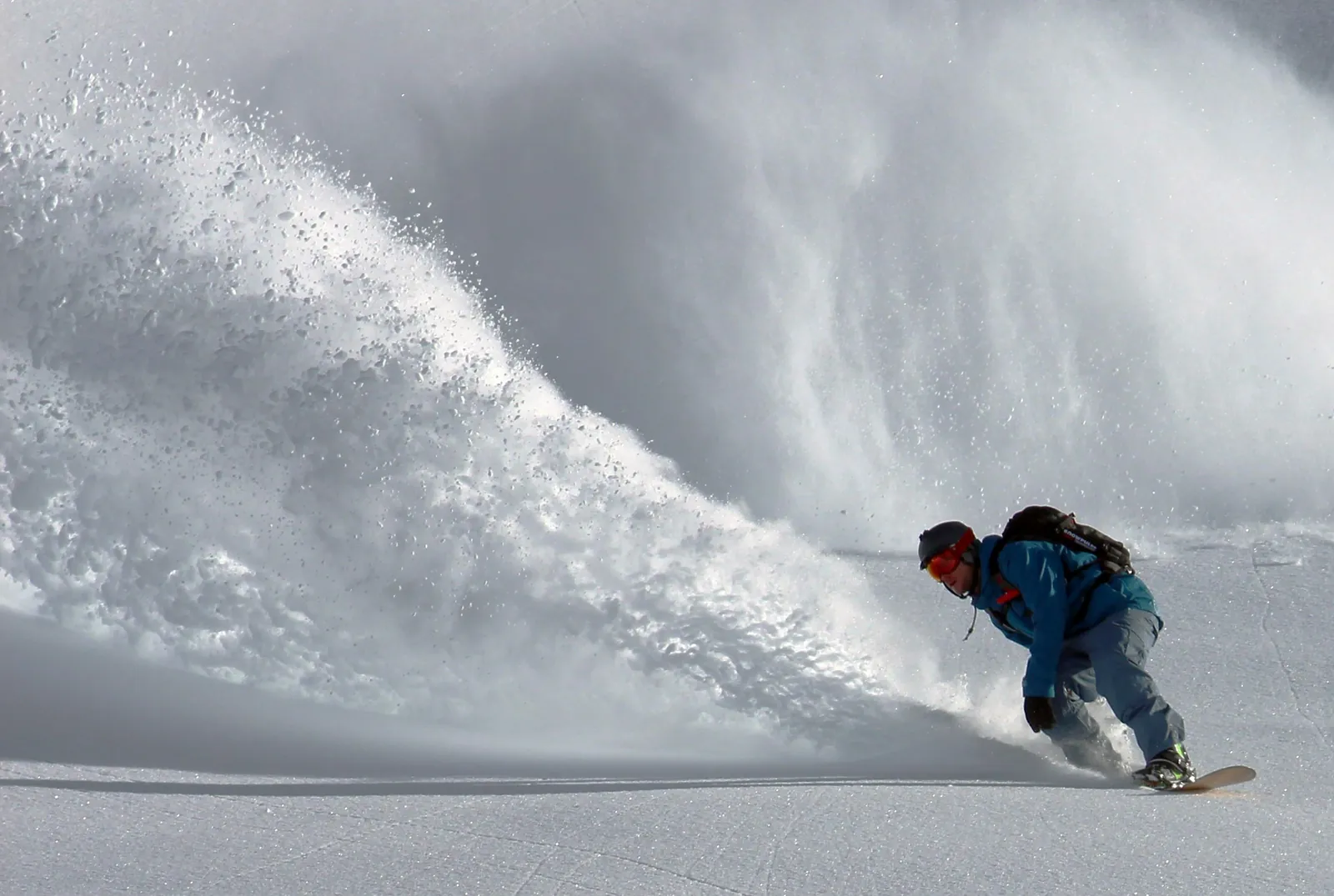 Snowboarder carving hard with a wave of powder arcing behind him